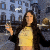 a woman in a yellow crop top is holding a glass of water and says yeah .