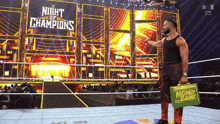 a wrestler is holding a money bank in front of a night of champions sign
