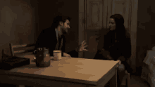 a man and a woman are sitting at a table with a mug on it