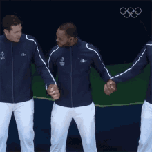 three men in lacoste jackets are holding hands in front of the olympic rings