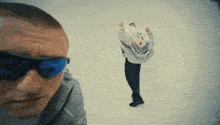a man wearing sunglasses looks at another man in a hoodie