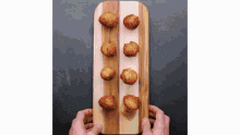 a person is holding a wooden cutting board with fried doughnuts on it .