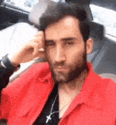 a man with a beard and a red jacket is sitting in a car .