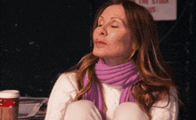 a woman wearing a white sweater and a purple scarf is sitting in front of a sign that says fire station