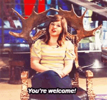 a woman is sitting in a chair with antlers on it and says you 're welcome