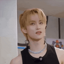 a young man with blonde hair wearing a black tank top and a silver chain around his neck