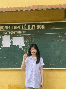a girl giving a peace sign in front of a bulletin board that says uong thpt le quy don