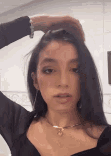 a woman wearing a black top and a gold necklace holds her hair