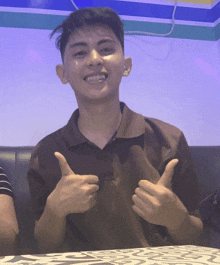 a young man giving a thumbs up while sitting on a couch
