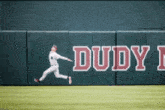 a baseball player jumps to catch a ball in front of a dudy wall