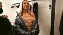 a woman is standing in a dressing room wearing a black jacket and a mask .