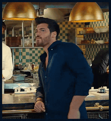 a man in a blue shirt is standing in a kitchen looking at something .