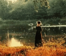 a woman in a black dress is standing in front of a body of water