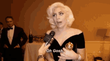 a woman in a black dress is talking into a microphone and holding a golden globe .