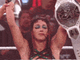 a woman in a wrestling ring holds up a championship belt with the letter x on it