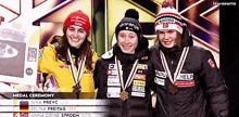 three female athletes are posing for a medal ceremony with one wearing a gorania hat