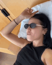 a woman wearing sunglasses is laying on a bed with her hand on her forehead