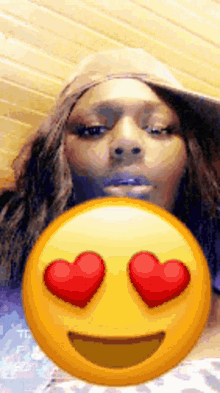 a woman wearing a hat is behind an emoji with hearts in its eyes