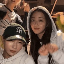 a woman wearing a ny hat stands next to another woman wearing a white hoodie