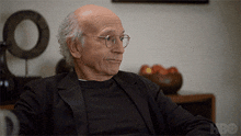 a man wearing glasses and a black shirt is sitting in front of an hbo sign