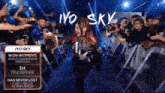a woman with red hair is walking through a crowd with a sign that says iyo sky
