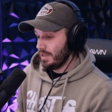 a man with a beard is wearing headphones and a hat while talking into a microphone .