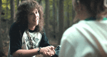 a man wearing a hellfire club shirt talks to another person