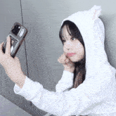a girl in a white hoodie taking a selfie with her phone