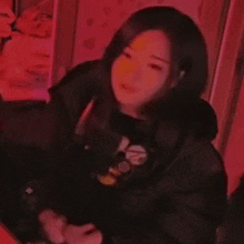 a woman in a black jacket is sitting in a dark room with red lights .