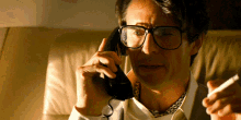a man wearing glasses is talking on a phone and smoking a cigarette
