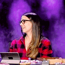 a woman wearing glasses sits in front of a laptop
