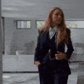 a woman in a suit is standing in a room with her hands in her pockets