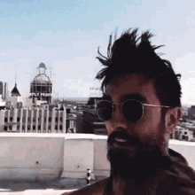 a man wearing sunglasses and a mohawk stands on a rooftop with a building in the background that says apply perm