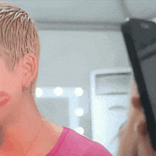 a woman wearing a pink shirt is looking at herself in a mirror