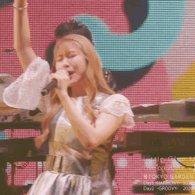 a woman singing into a microphone with her arms up