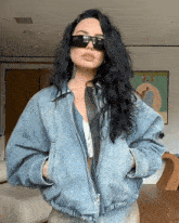 a woman wearing sunglasses and a denim jacket is standing in a living room