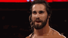 a man with long hair and a beard is smiling in front of a red background