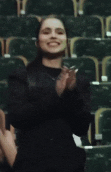 a woman in a black jacket is clapping her hands in a stadium
