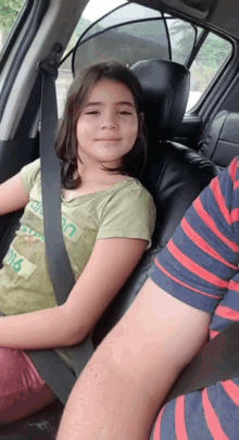 a girl wearing a green shirt that says ' california ' on it sits in a car seat