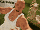 a bald man wearing a white tank top and a cross necklace stands in front of a sign that says ' jano '