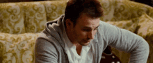 a man is sitting on a couch wearing a gray hoodie and a white shirt .