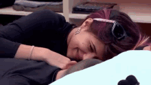 a man and a woman are laying on a bed . the woman is wearing sunglasses and a black shirt .