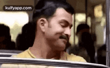 a man with a mustache is sitting on a bus with his eyes closed .