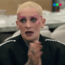 a woman with a shaved head and pink eyebrows is clapping