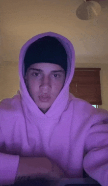 a young man wearing a pink hoodie and a black hat is sitting at a table .