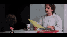 a woman sits at a desk holding a piece of paper and a cup that says ' coca cola '