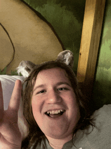a young girl wearing a wolf headband is smiling and giving the peace sign