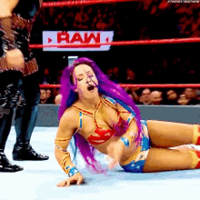 a woman with purple hair is laying on the ground in a wrestling ring in front of a raw sign