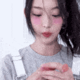 a close up of a woman wearing overalls and a gray shirt holding a pink object in her hands .