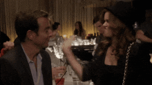 a woman in a black hat is pointing at a man with playing cards in front of his face